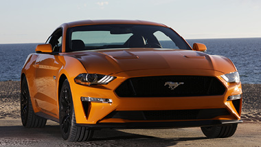 A yellow orange Mustang stands proudly in front of the blue ocean
